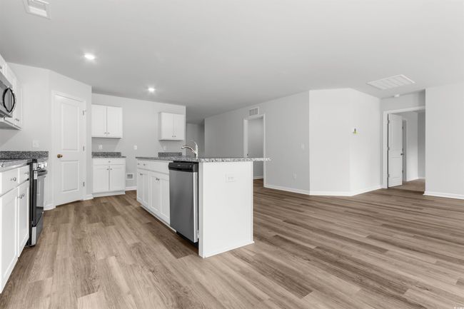 Kitchen featuring light stone countertops, light wood-type flooring, an island with sink, white cabinetry, and stainless steel appliances | Image 16