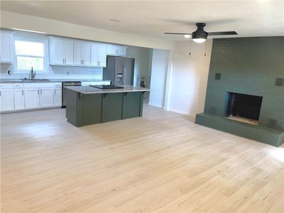 Living room with a brick fireplace, light wood-type flooring, ceiling fan, and sink | Image 3