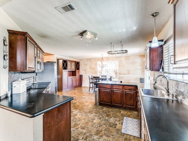 Kitchen with a peninsula, stainless steel appliances, a textured ceiling, pendant lighting, and dark countertops | Image 4