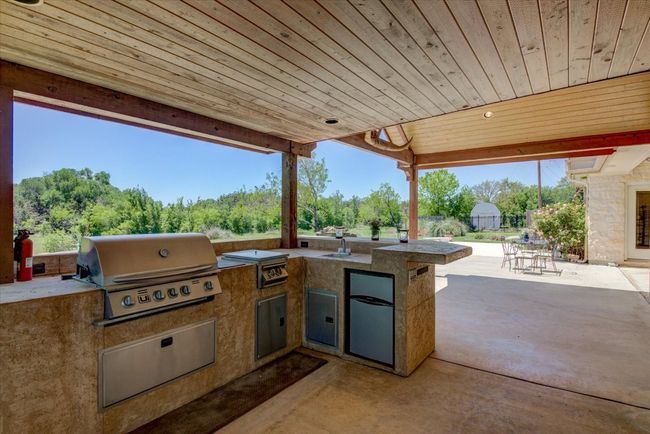 Outdoor kitchen features a grill, sink, refrigerator, and a view of the pool. | Image 31