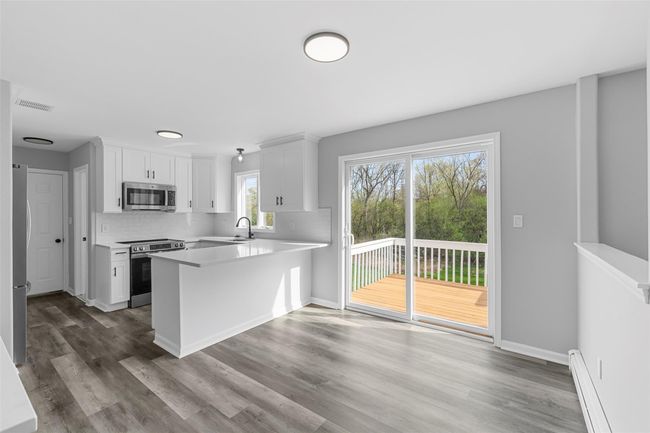 Kitchen with appliances with stainless steel finishes, light countertops, baseboard heating, wood finished floors, and a peninsula | Image 8
