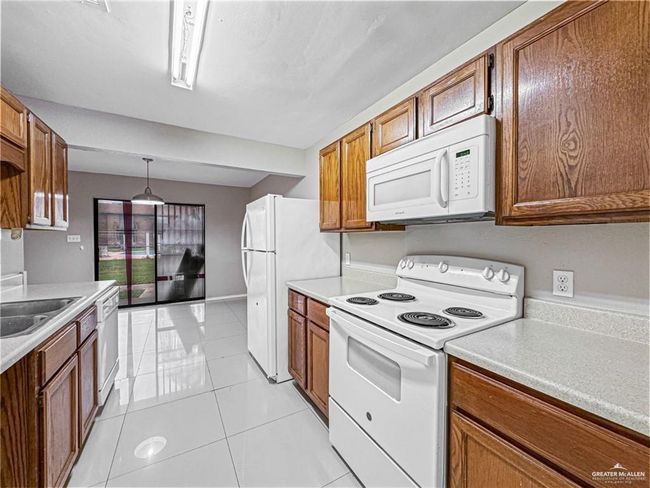 Kitchen featuring white appliances, light tile patterned flooring, decorative light fixtures, and sink | Image 6