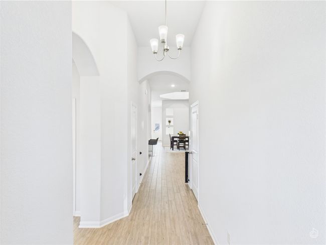 Hall with a chandelier, arched walkways, light wood-style floors, baseboards, and a high ceiling | Image 6