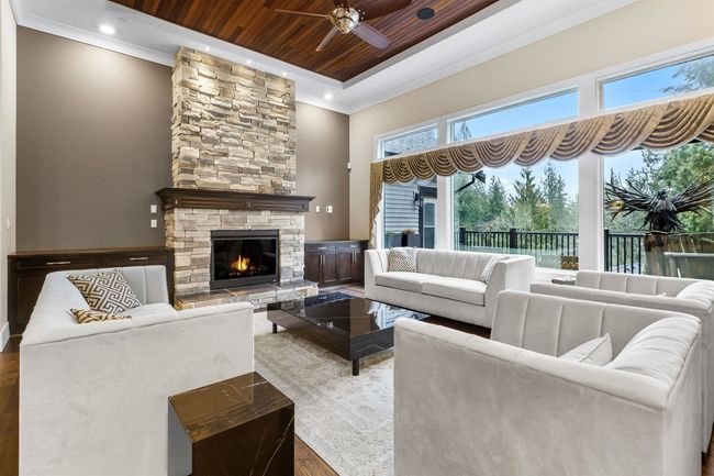 Living room with wooden ceiling, a tray ceiling, crown molding, a stone fireplace, and recessed lighting | Image 7