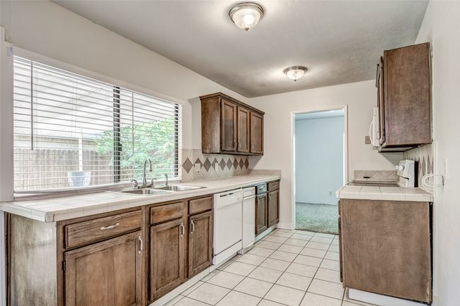 Kitchen with a sink, white appliances, light tile patterned floors, decorative backsplash, and tile countertops | Image 10