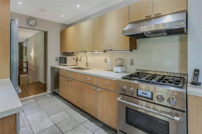 Kitchen featuring under cabinet range hood, appliances with stainless steel finishes, a sink, light countertops, and light tile patterned flooring | Image 17