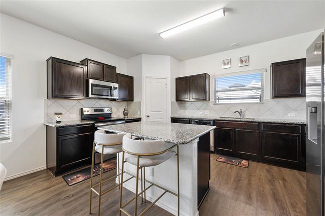 Kitchen with appliances with stainless steel finishes, a center island, dark wood-style flooring, and a breakfast bar area | Image 6