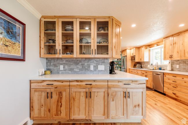 Kitchen featuring light brown cabinets, glass insert cabinets, light countertops, backsplash, and appliances with stainless steel finishes | Image 6