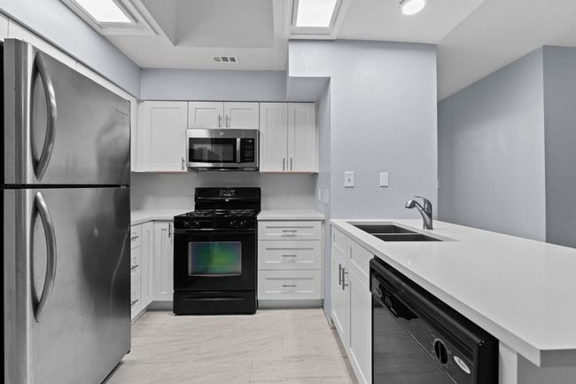 Kitchen featuring black appliances, light countertops, light marble finish flooring, and white cabinets | Image 17
