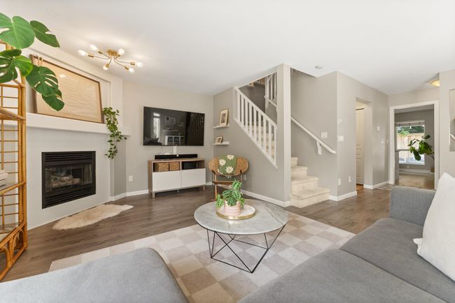 Living room with wood finished floors, stairs, a glass covered fireplace, and baseboards | Image 11
