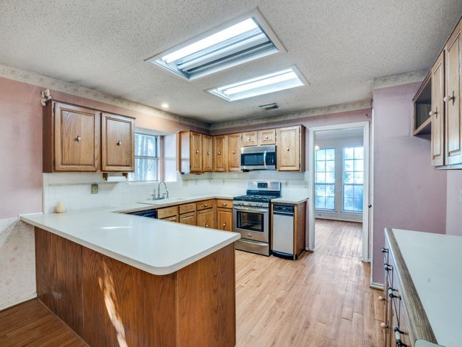 Kitchen featuring appliances with stainless steel finishes, a textured ceiling, a peninsula, light wood-style floors, and a sink | Image 6