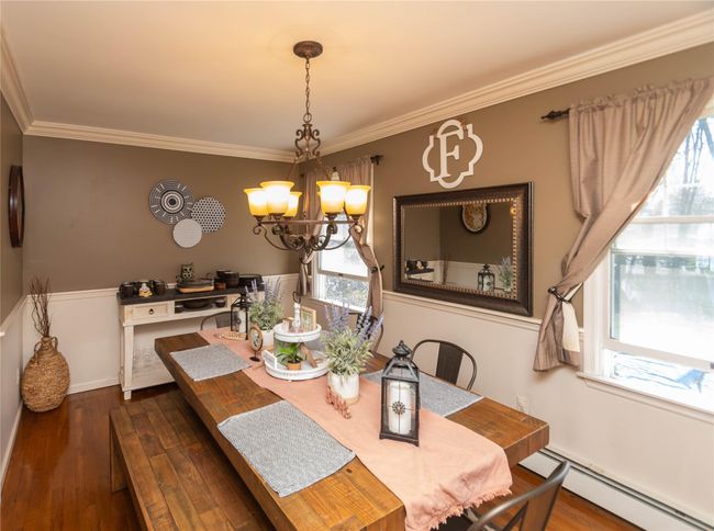 Dining area with a chandelier, wood finished floors, ornamental molding, baseboards, and a baseboard radiator | Image 6