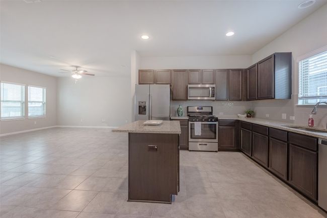 Kitchen featuring light stone counters, a kitchen island, a sink, ceiling fan, and stainless steel appliances | Image 37