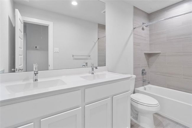 Secondary bath features tile flooring, bath/shower combo with tile surround, stained cabinets, beautiful light countertops, dual vanities, mirror, sleek fixtures and modern finishes. | Image 16