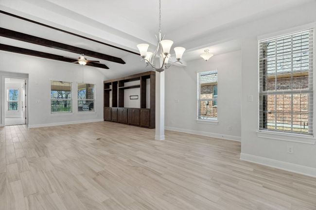 Unfurnished living room with baseboards, light wood-style floors, vaulted ceiling with beams, and ceiling fan with notable chandelier | Image 6