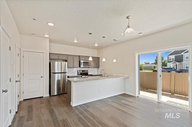 Kitchen featuring appliances with stainless steel finishes, backsplash, pendant lighting, a peninsula, and light stone countertops | Image 6