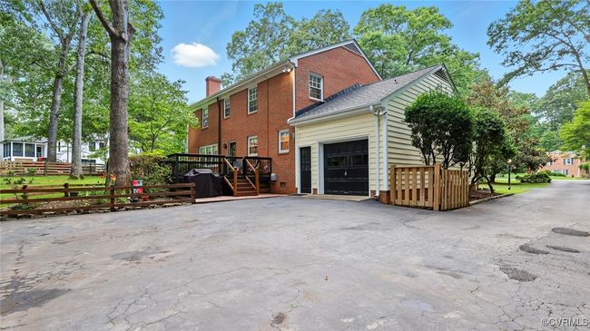 View of side of home with an attached garage, a deck, brick siding, asphalt driveway, and a chimney | Image 14