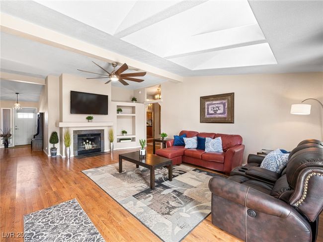 Living area with vaulted ceiling with skylight, a fireplace, wood finished floors, and a ceiling fan | Image 11