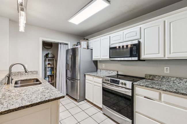 Kitchen featuring stainless steel appliances, light stone countertops, light tile patterned flooring, and white cabinets | Image 6