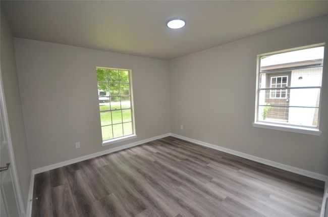 This bedroom is bright and welcoming, featuring large windows that let in natural light, light gray walls, and modern wood-like flooring. | Image 17
