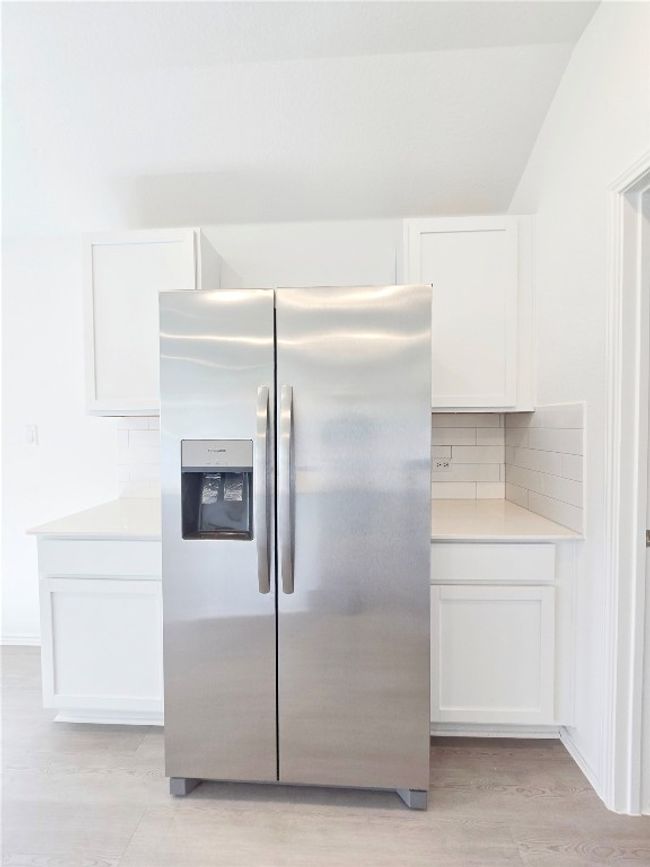 Kitchen featuring stainless steel fridge, white cabinets, backsplash, light countertops, and light wood-style floors | Image 22