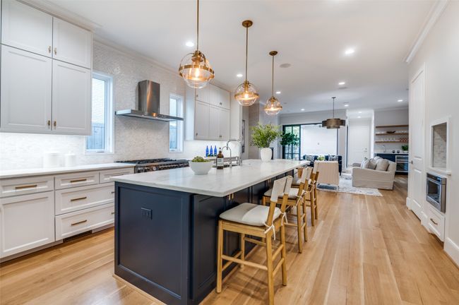 Kitchen with white cabinets, light wood finished floors, wall chimney exhaust hood, a center island with sink, and appliances with stainless steel finishes | Image 8
