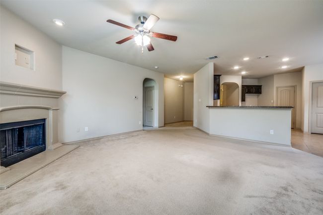 Unfurnished living room featuring ceiling fan, arched walkways, a fireplace with raised hearth, light carpet, and recessed lighting | Image 5