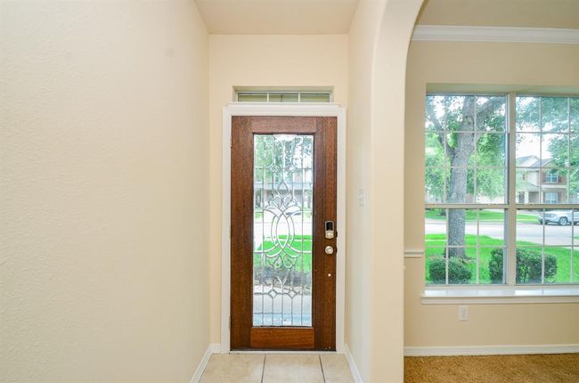 Bright and welcoming entryway featuring a decorative glass front door and large window, offering plenty of natural light and a view of the front yard. | Image 5