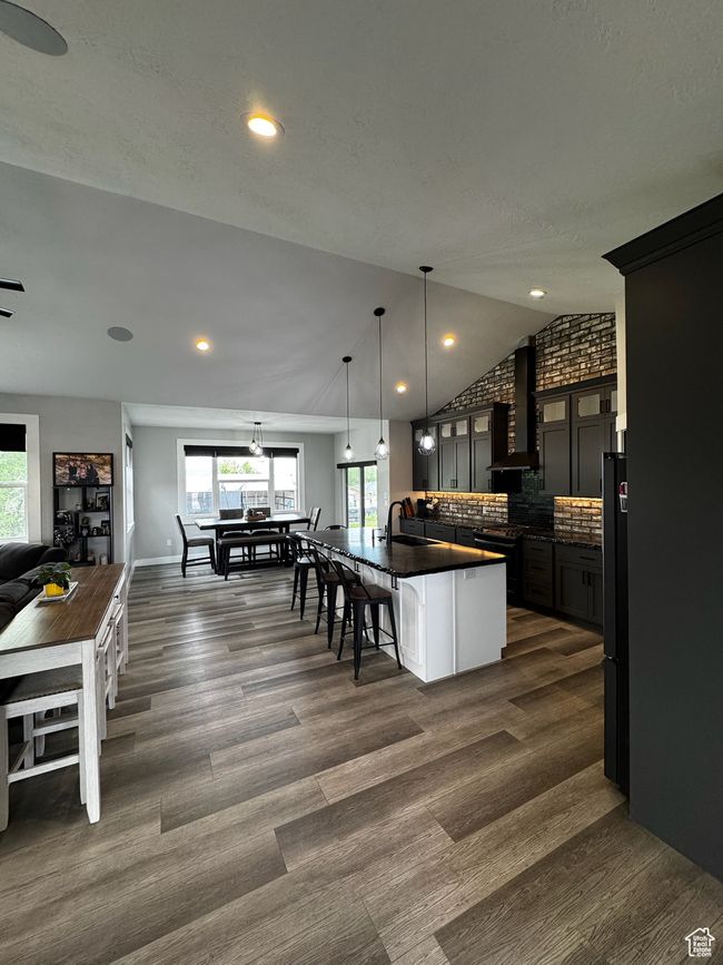 Kitchen featuring dark countertops, a sink, wall chimney range hood, plenty of natural light, and lofted ceiling | Image 4