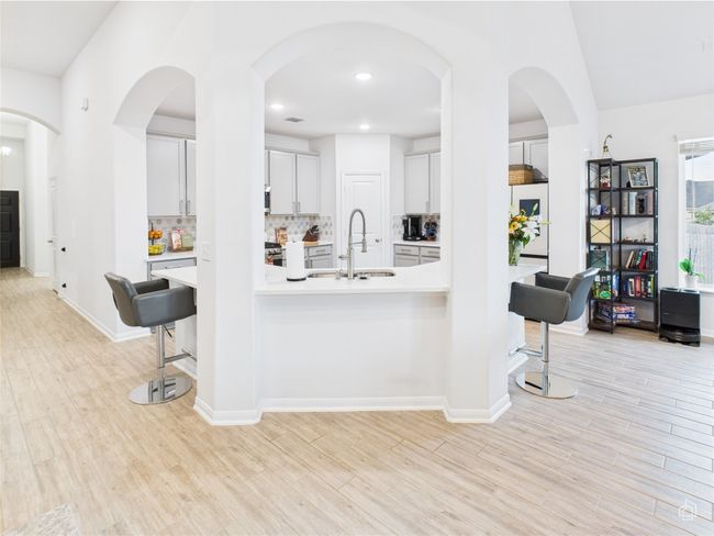 Kitchen with a sink, a breakfast bar, light countertops, light wood-type flooring, and decorative backsplash | Image 7