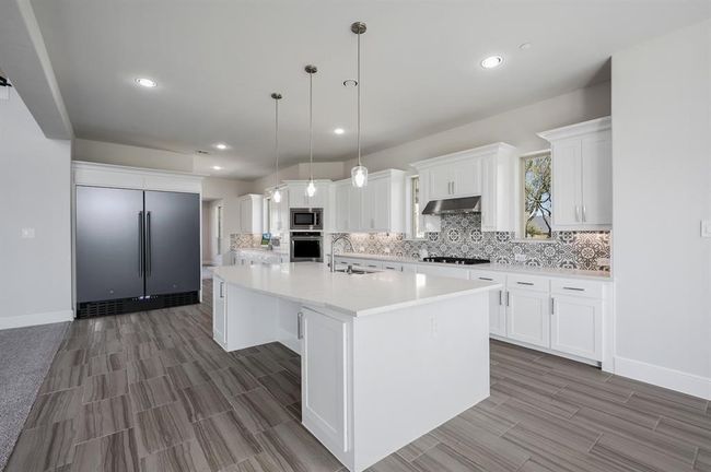 Kitchen with built in appliances, under cabinet range hood, decorative backsplash, a sink, and light countertops | Image 6