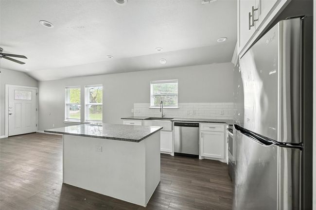 Kitchen featuring stainless steel appliances, white cabinets, backsplash, dark stone counters, and a kitchen island | Image 7