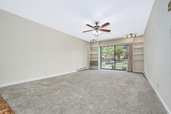 Carpeted living room featuring a ceiling fan, a baseboard heating unit, and cooling unit | Image 4
