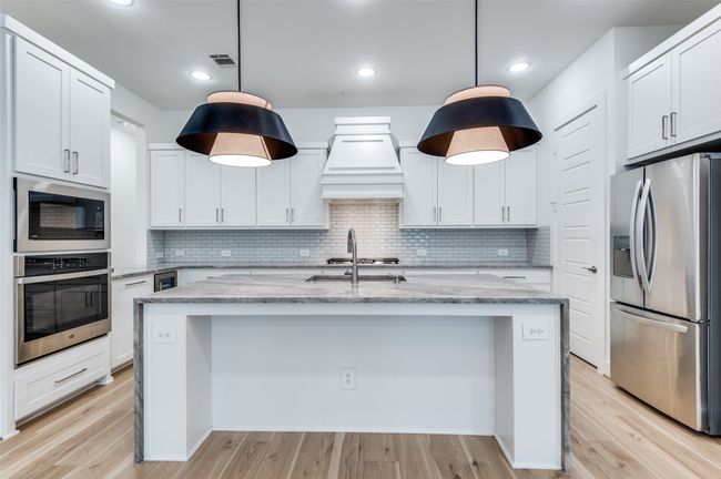 Kitchen with premium range hood, stainless steel appliances, waterfall island and luxury lighting | Image 4