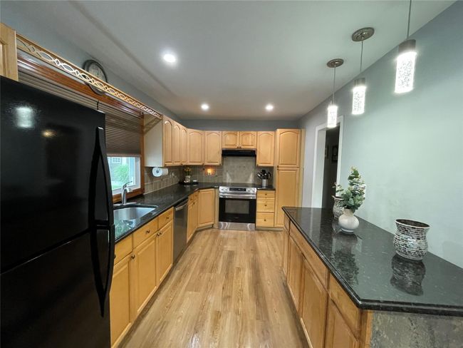 Kitchen with stainless steel appliances, light wood-type flooring, under cabinet range hood, a sink, and tasteful backsplash | Image 17