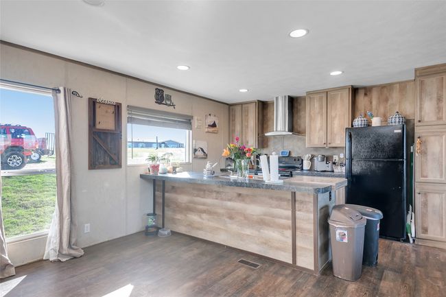 Kitchen featuring a wealth of natural light, dark wood-style floors, black appliances, and wall chimney exhaust hood | Image 19
