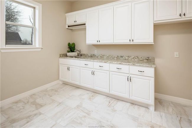 Kitchen with light stone counters, a sink, marble finish floor, white cabinetry, and baseboards | Image 22