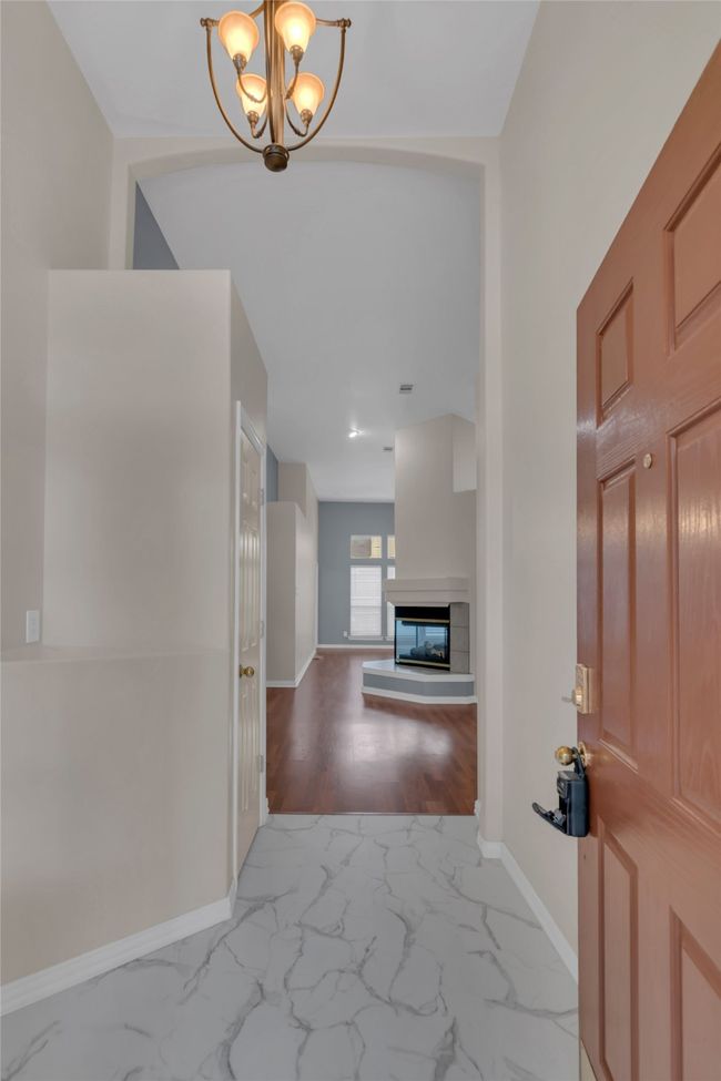 Entryway featuring marble look tile flooring, a chandelier, and a glass covered fireplace | Image 6