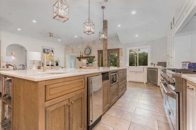 Kitchen with stainless steel appliances, light countertops, recessed lighting, pendant lighting, and a kitchen island with sink | Image 12