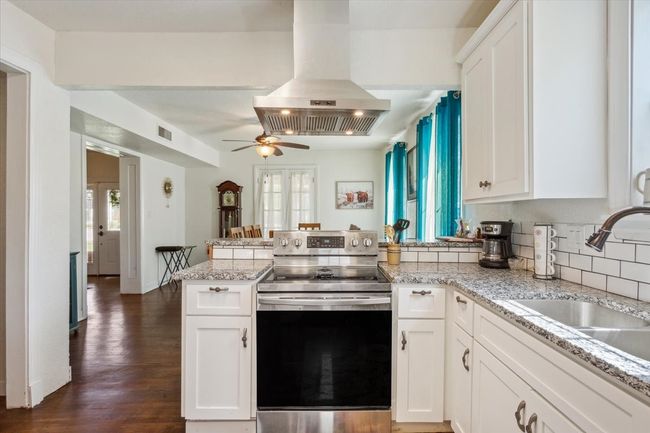 Kitchen featuring stainless steel electric stove, a peninsula, visible vents, island exhaust hood, and a sink | Image 13