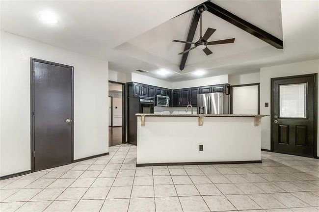 Kitchen with lofted ceiling with beams, light stone counters, stainless steel appliances, a sink, and a kitchen breakfast bar | Image 16