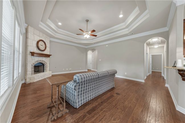 Living area with arched walkways, ceiling fan, hardwood / wood-style floors, a raised ceiling, and a stone fireplace | Image 7