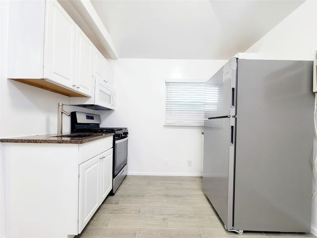 Kitchen with freestanding refrigerator, stainless steel gas range oven, white cabinets, baseboards, and dark stone counters | Image 5