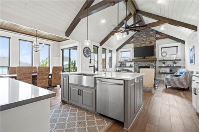 Kitchen with pendant lighting, an island with sink, a stone fireplace, stainless steel dishwasher, and gray cabinetry | Image 3