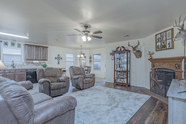 Living area featuring ceiling fan with notable chandelier, a fireplace, visible vents, and dark wood-type flooring | Image 7