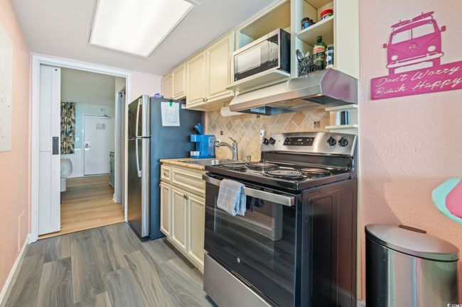 Kitchen with cream cabinets, appliances with stainless steel finishes, decorative backsplash, ventilation hood, and wood finished floors | Image 8