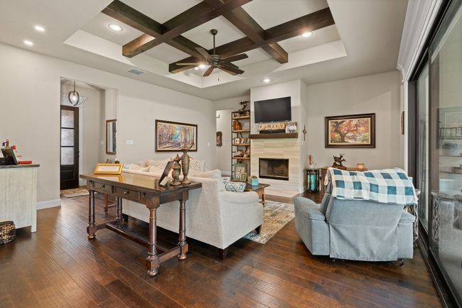 Living room featuring coffered ceiling, dark wood-style floors, a ceiling fan, a tile fireplace, and beamed ceiling | Image 6