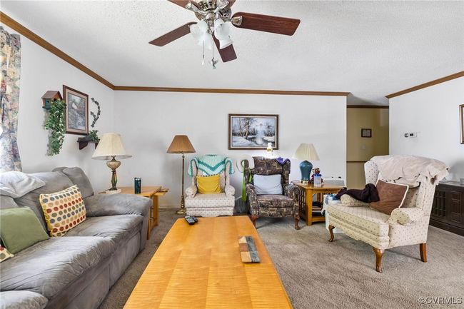 Carpeted living area with a textured ceiling, crown molding, and a ceiling fan | Image 7