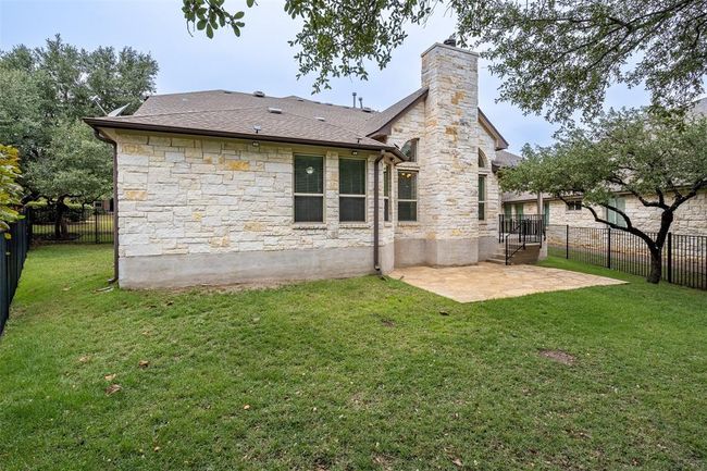 Back of property featuring stone siding, a patio, a fenced backyard, and a chimney | Image 23