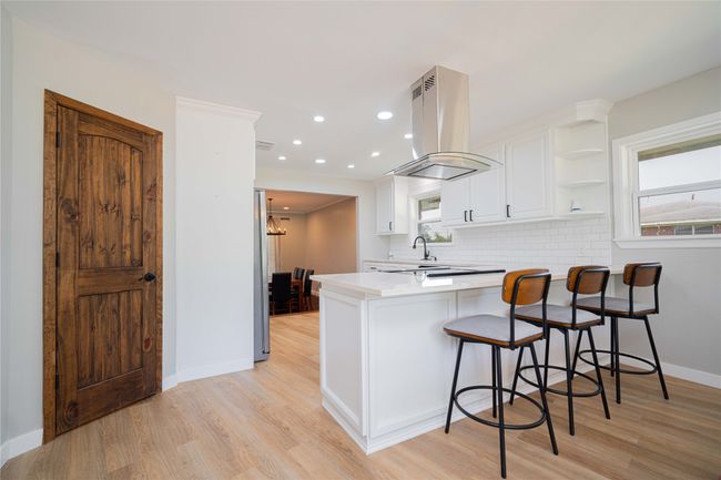 Kitchen with island range hood, a peninsula, light wood finished floors, white cabinetry, and recessed lighting | Image 15